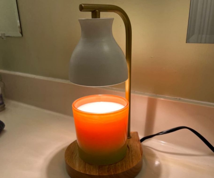 A candle in a warmer lamp on a counter