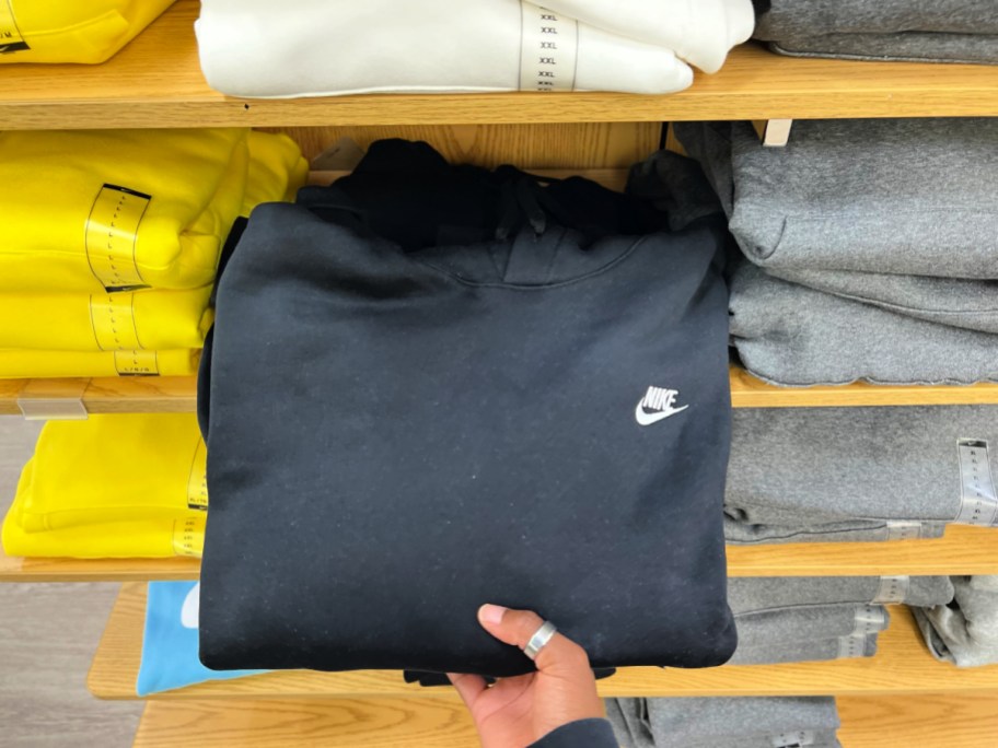 Women taking black Nike hoodie off of wooden store shelf