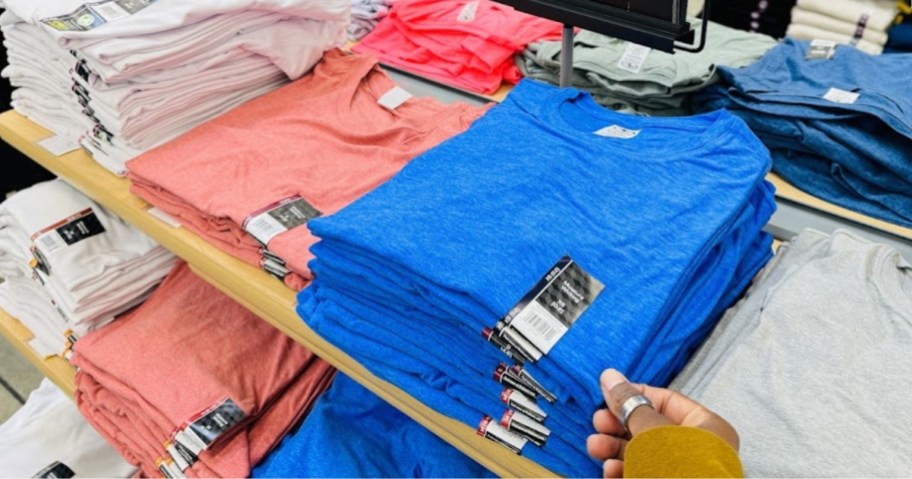 hand reaching for a blue t-shirt on a Walmart display with other colors of t-shirts